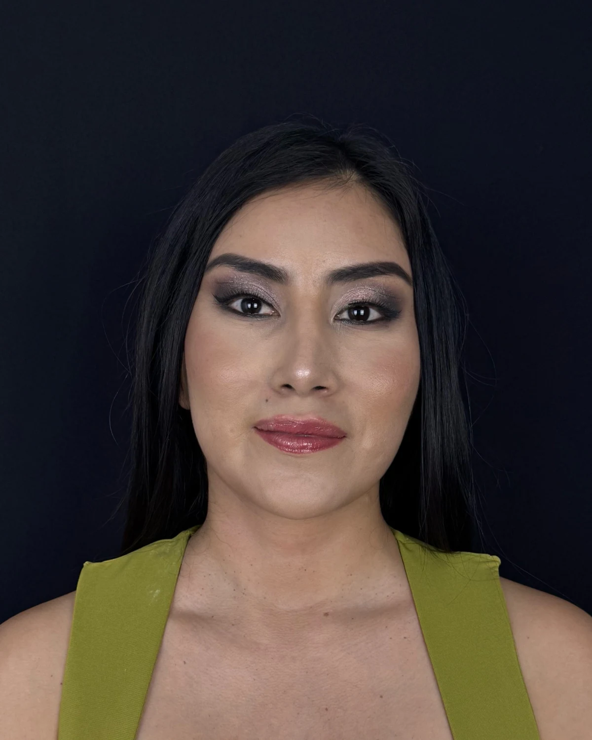 La misma paciente de frente después del lifting endoscópico, con vestido verde oliva sobre fondo oscuro